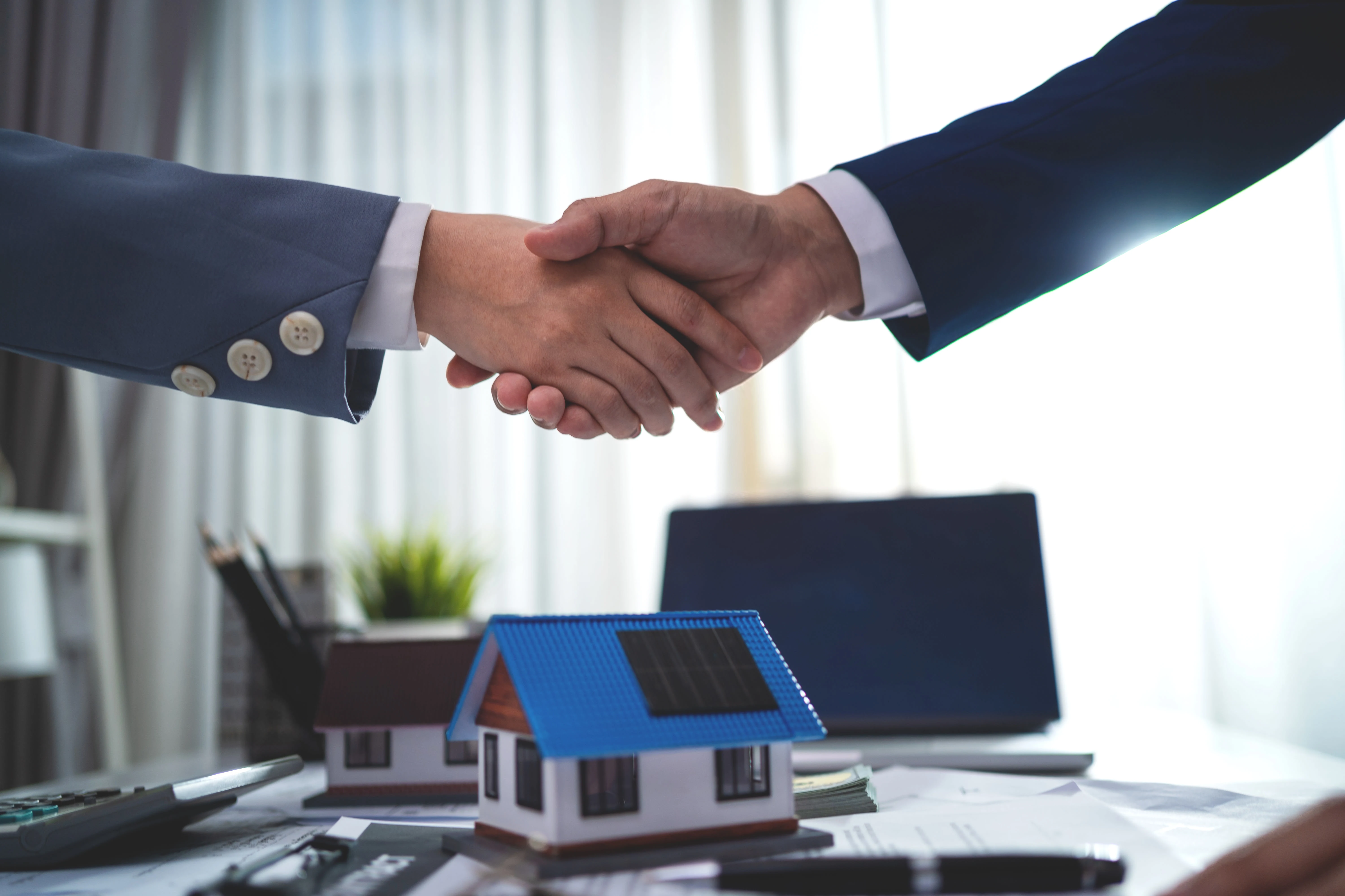 Handshake over house models, representing property loan agreement