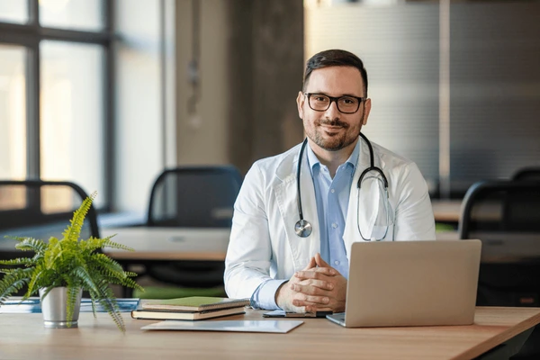 Male doctor sitting at desk holding heart model
